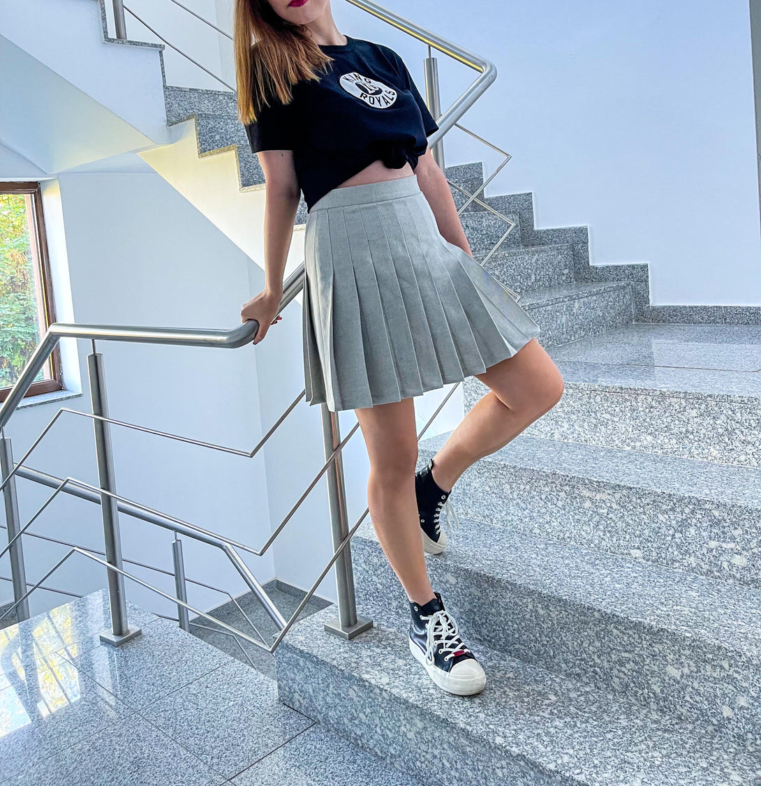 woman sporting a grey pleated skirt and converse sneakers